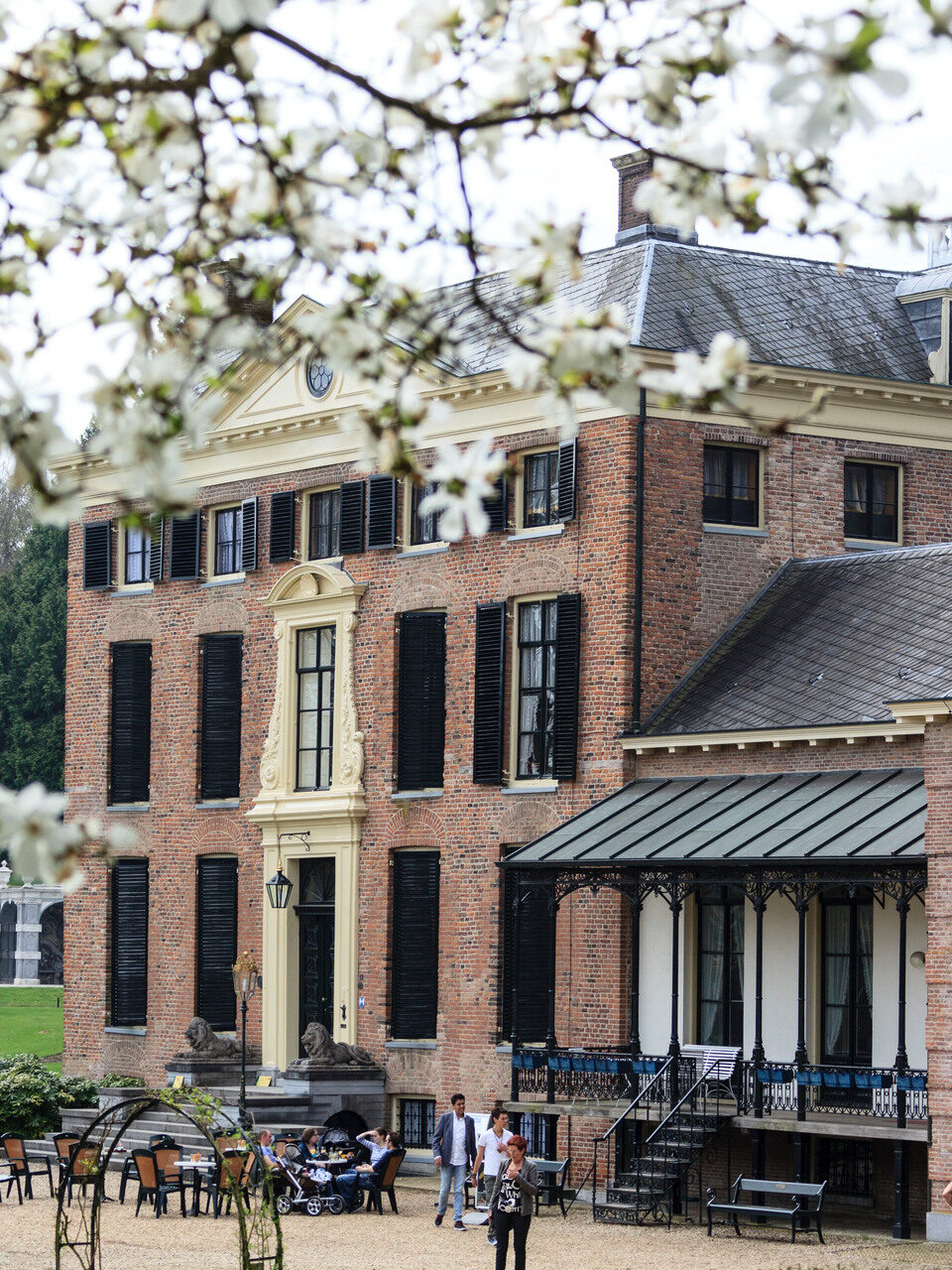 Mensen op het terras voor Kasteel Rosendael, op de voorgrond bloeit de bloesem in de boom