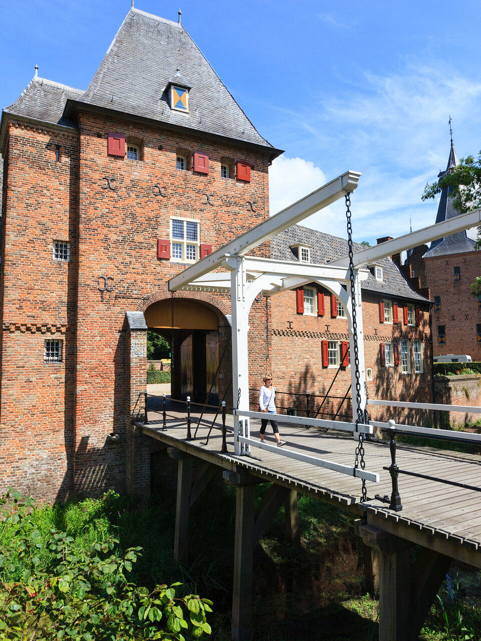 Een vrouw loopt over de ophaalbrug bij de ingang van kasteel Doorwerth