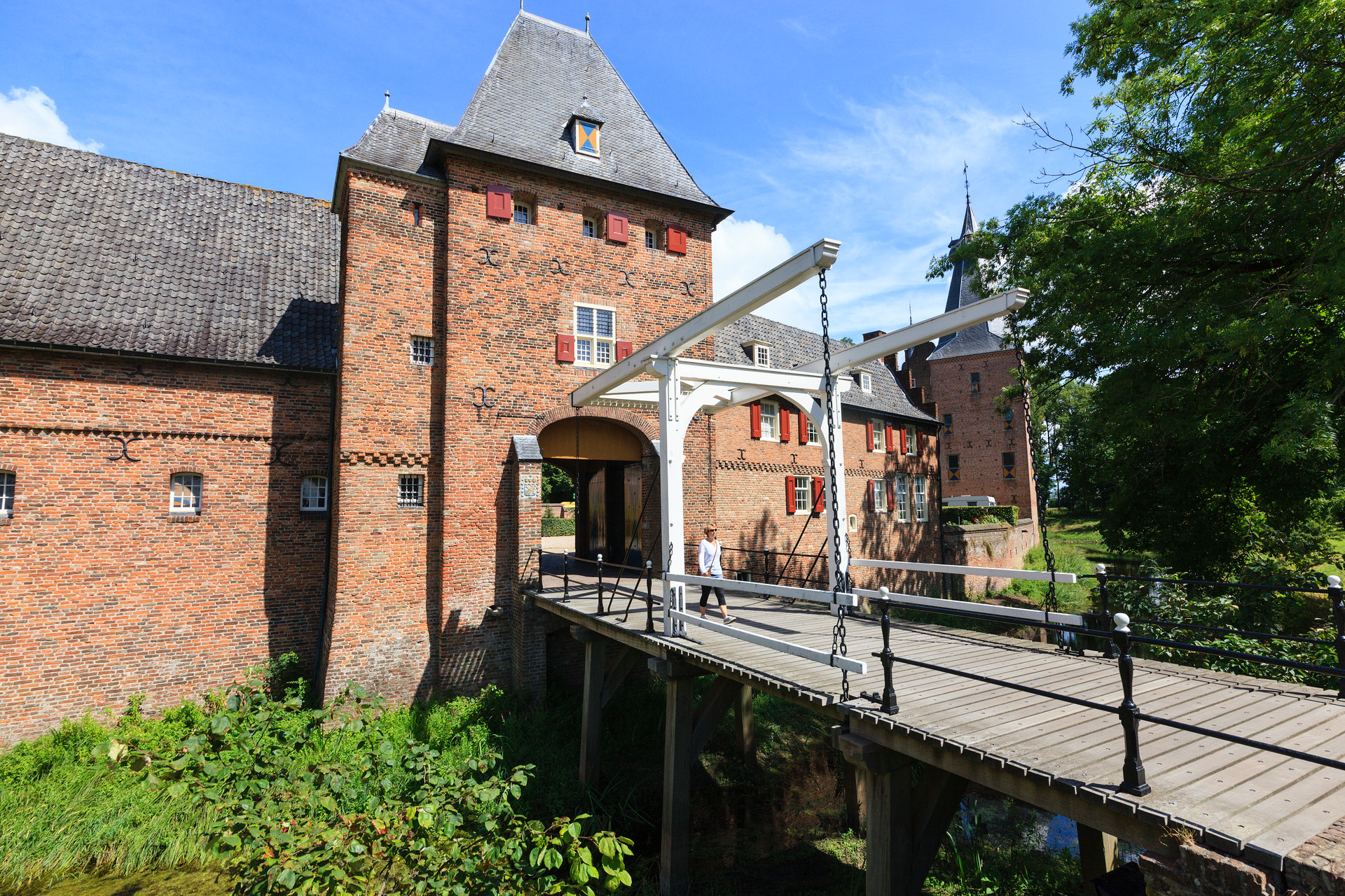 Een vrouw loopt over de ophaalbrug bij de ingang van kasteel Doorwerth