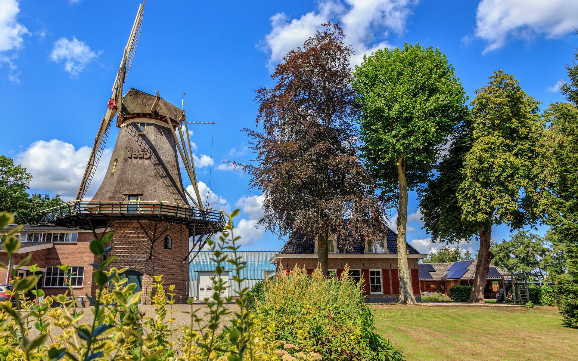 Molen op een zonnige dag, ernaast staat een huis met een tuin