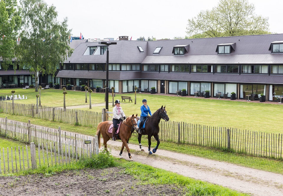 Ruiters rijden op hun paarden langs een hotel.