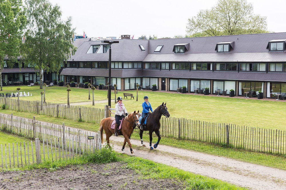 Ruiters rijden op hun paarden langs een hotel.