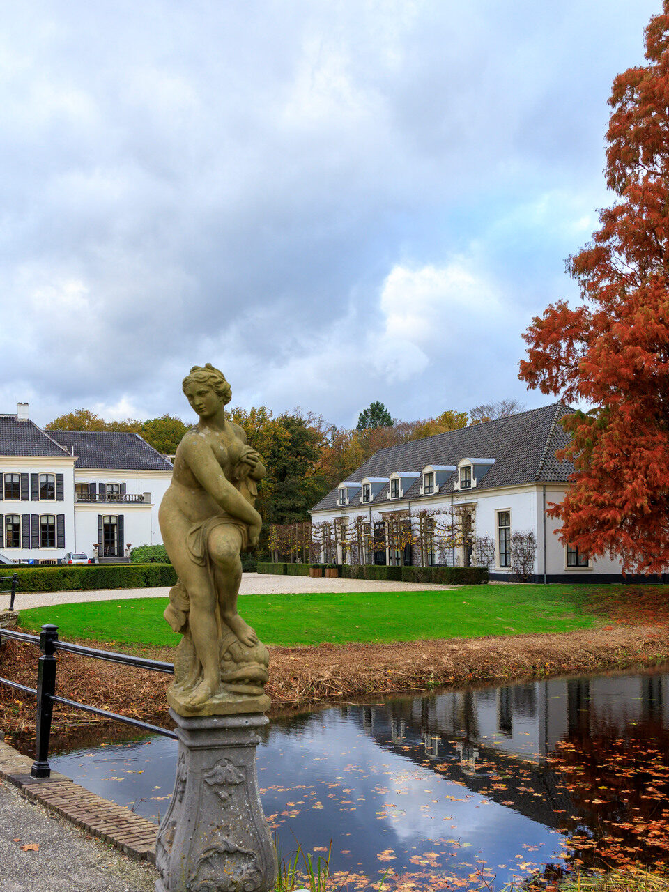 Een wit kasteel met vooraan een standbeeld een vijver.