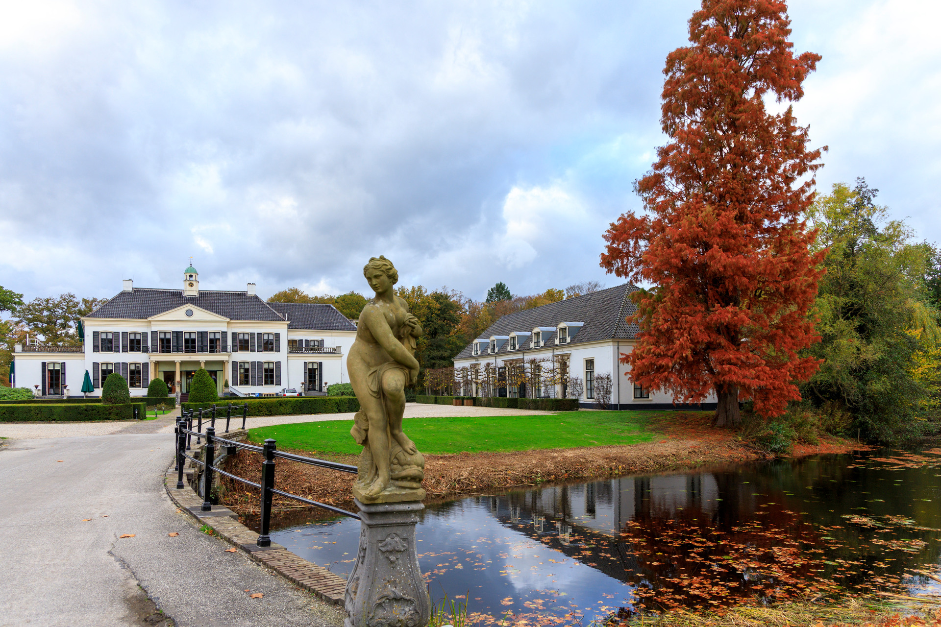 Een wit kasteel met vooraan een standbeeld een vijver.