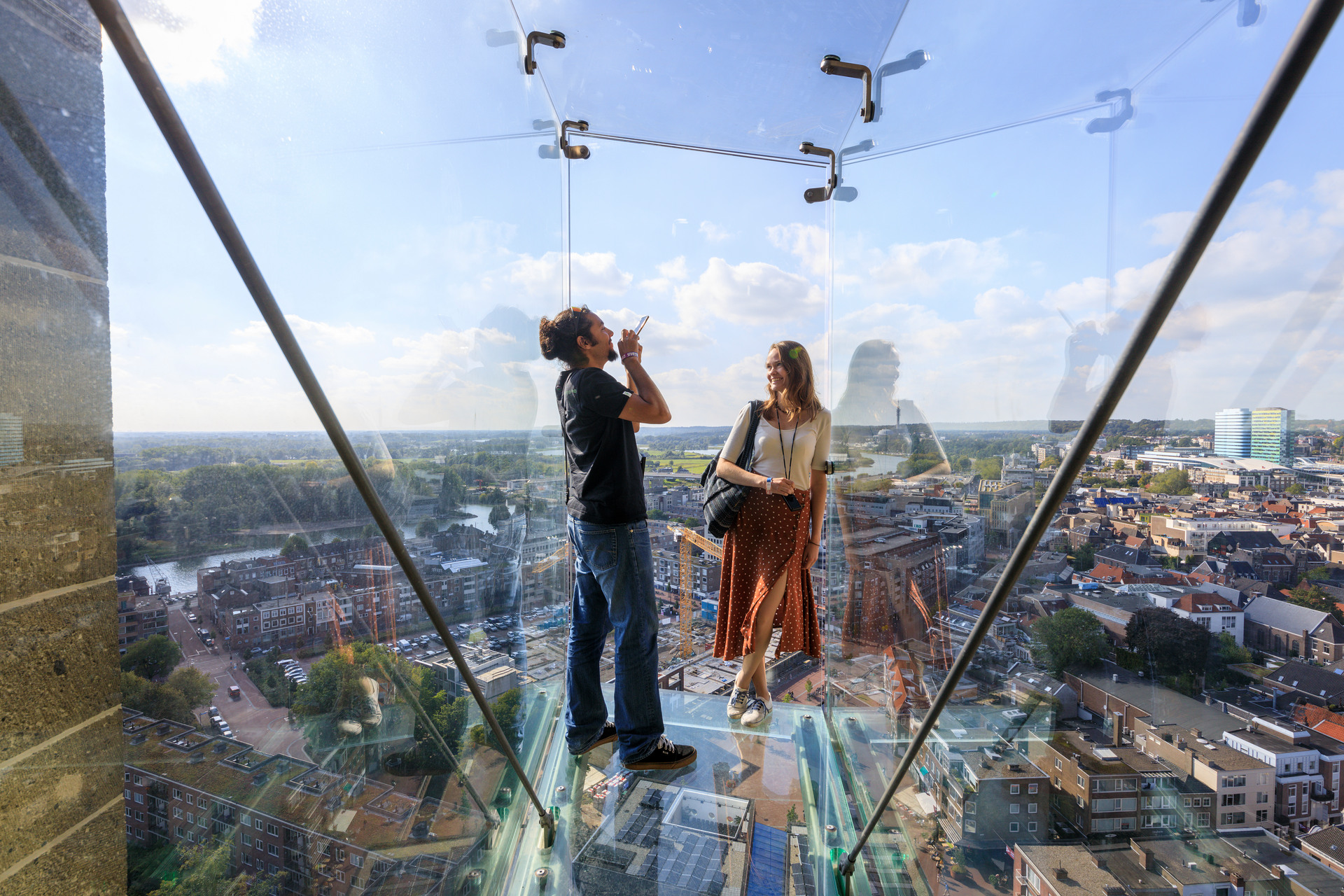 Een man maakt een foto van een vrouw terwijl ze op de glazen balkons van de Eusebiuskerk staan, met uitzicht op Arnhem