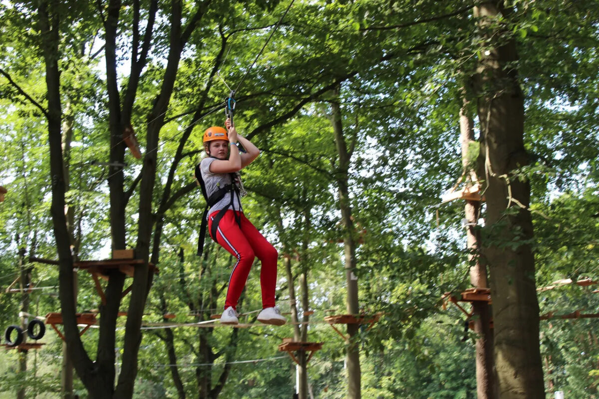 Meisje in rode broek en helm op klimparcours in het bos