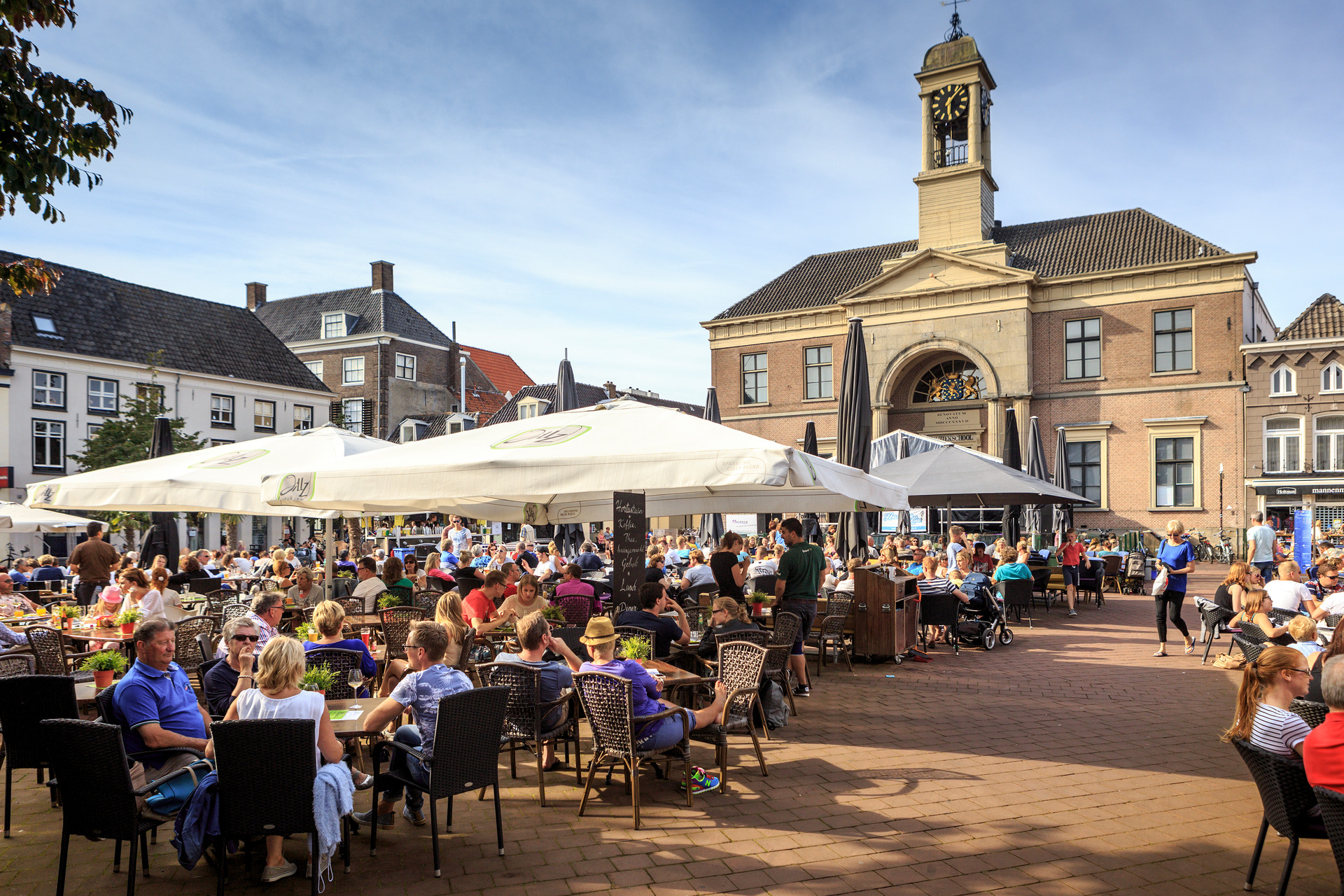 Groot gebouw van baksteen met terras vol mensen in de zomer