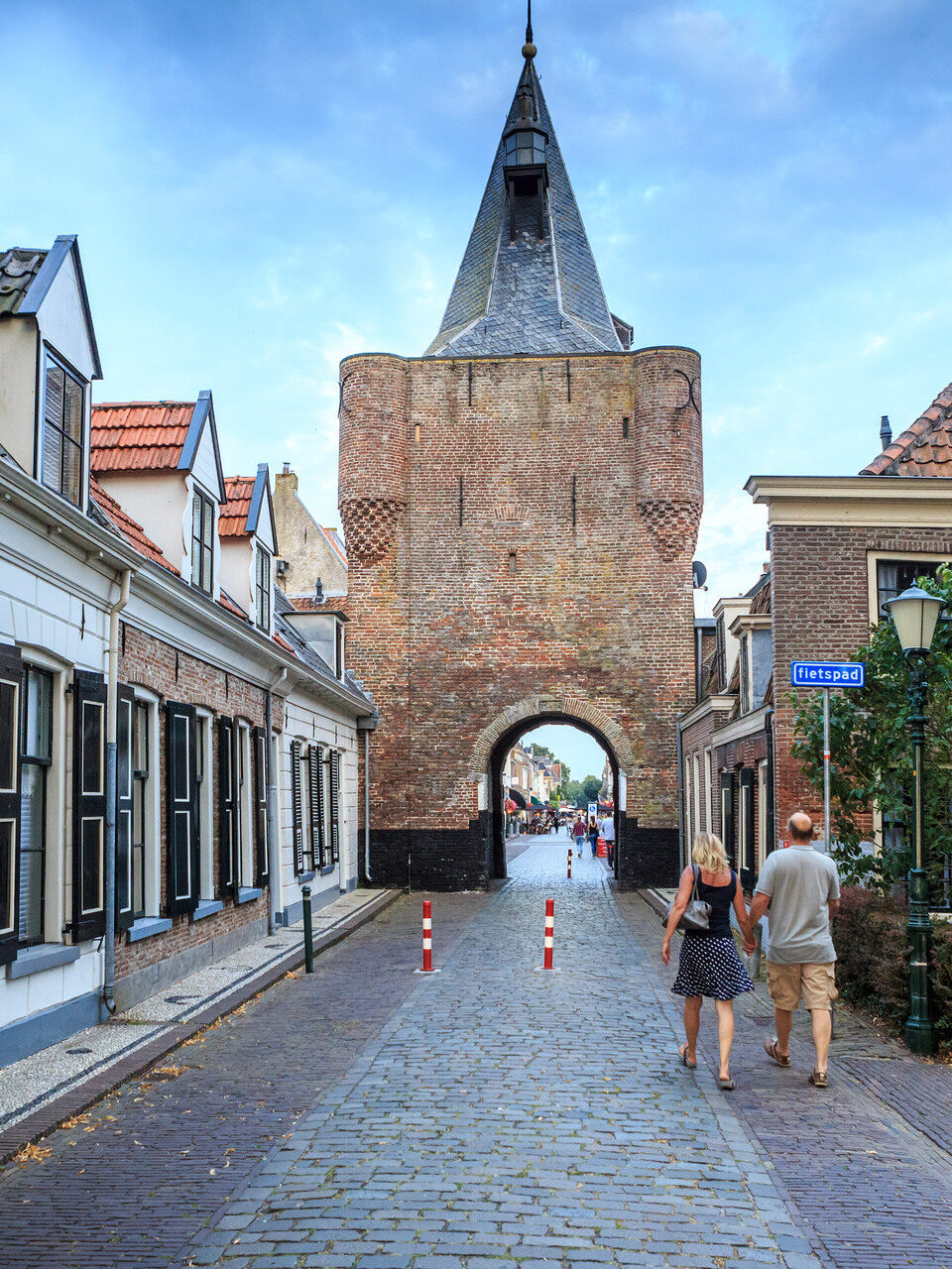 Een paar wandelt hand in hand over een kasseienstraat richting kasteel