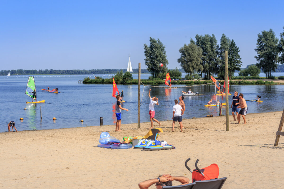 Mensen genieten van het mooie weer op het strand aan het Veluwemeer.