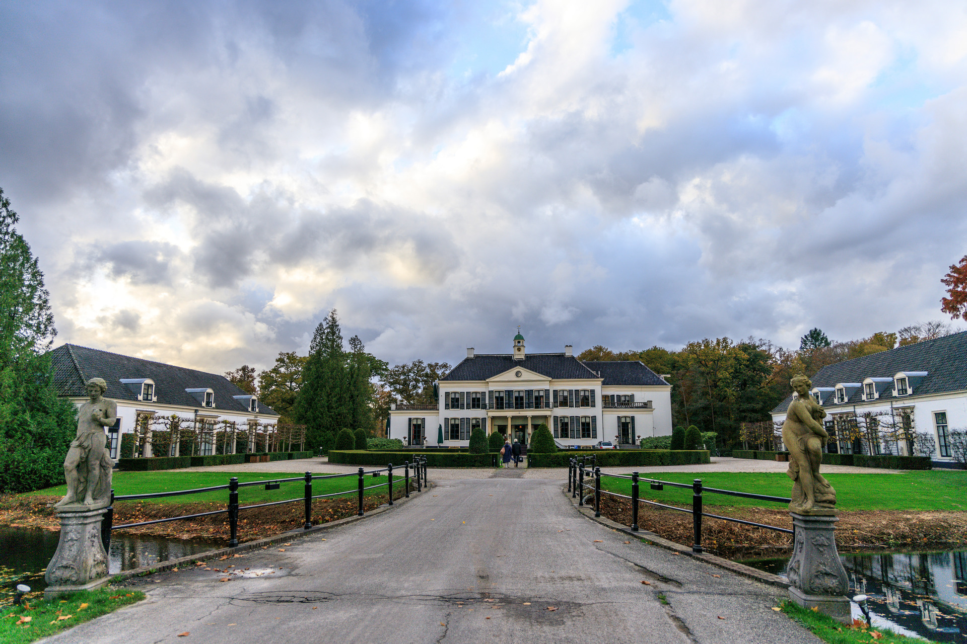 Een wit kasteel met vooraan een standbeeld een vijver.