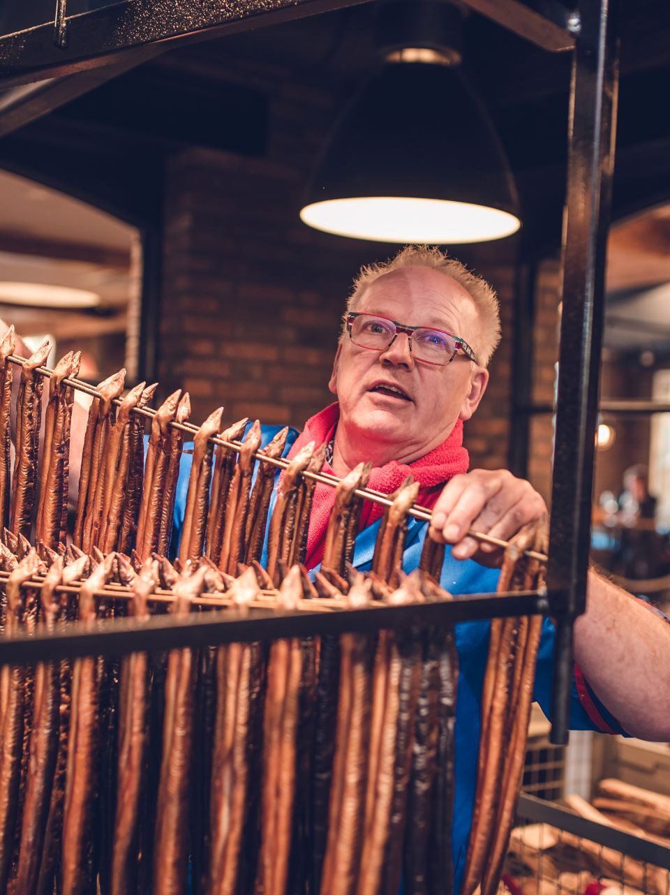 Meneer met bril in een palingrokerij. Voor zich hangen rijen vol palingen.