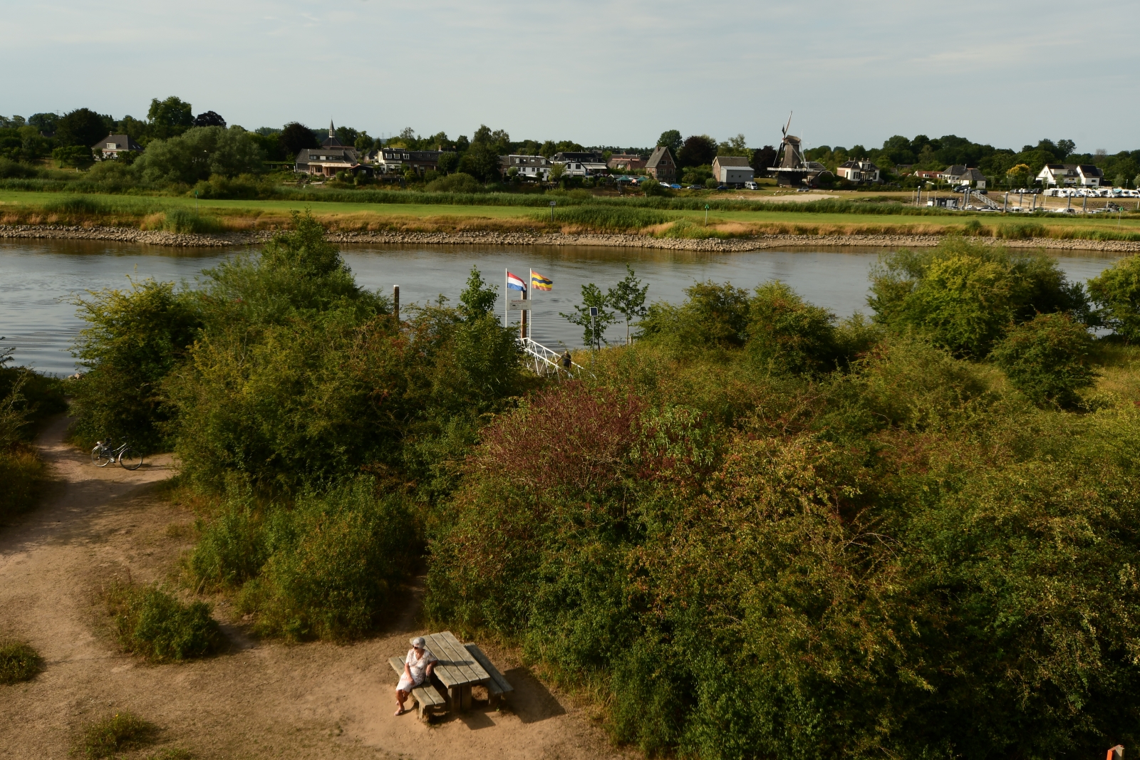 Vrouw op bankje tussen de bomen langs de IJssel en aan de overkant Veessen - vanaf uitkijktoren Fortmond.