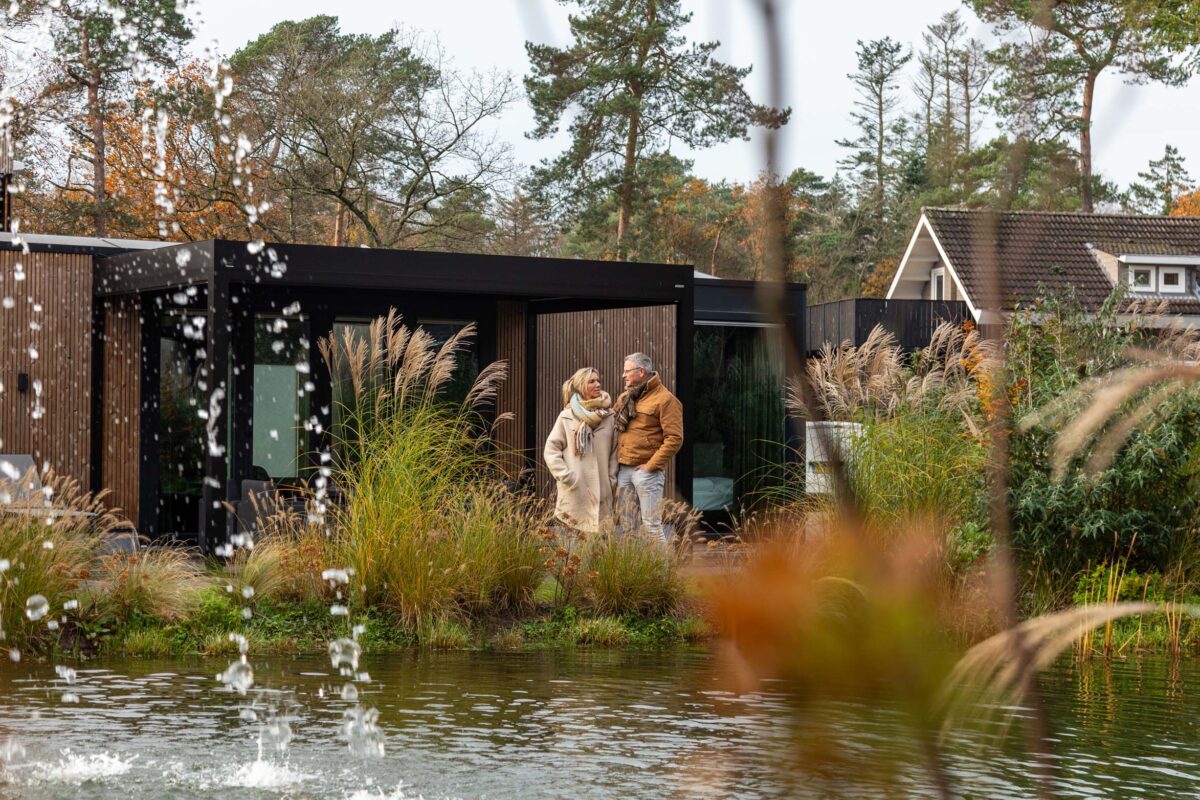 Een man en een vrouw staan voor een houten vakantiehuisje aan het water.