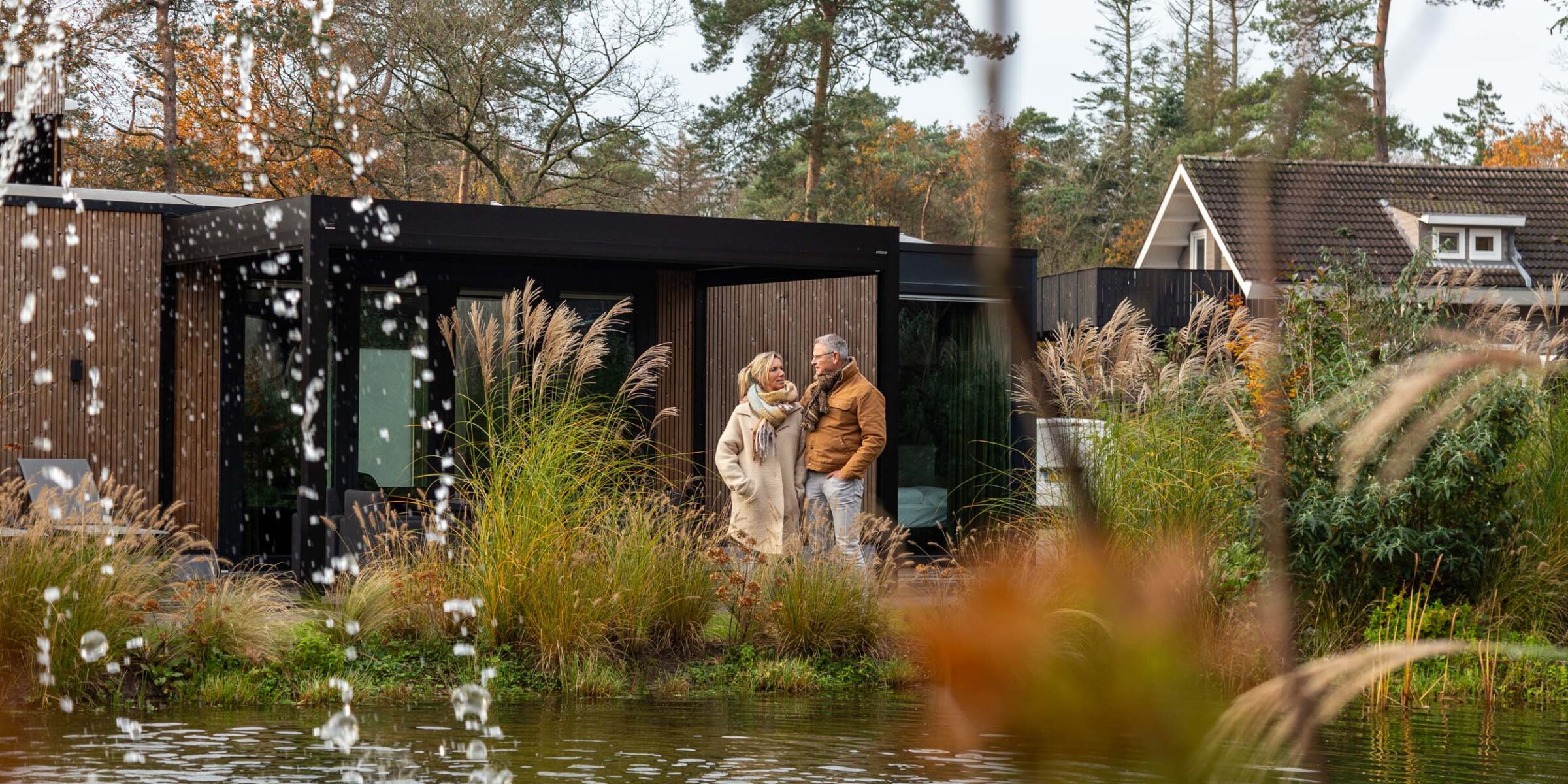 Een man en een vrouw staan voor een houten vakantiehuisje aan het water.