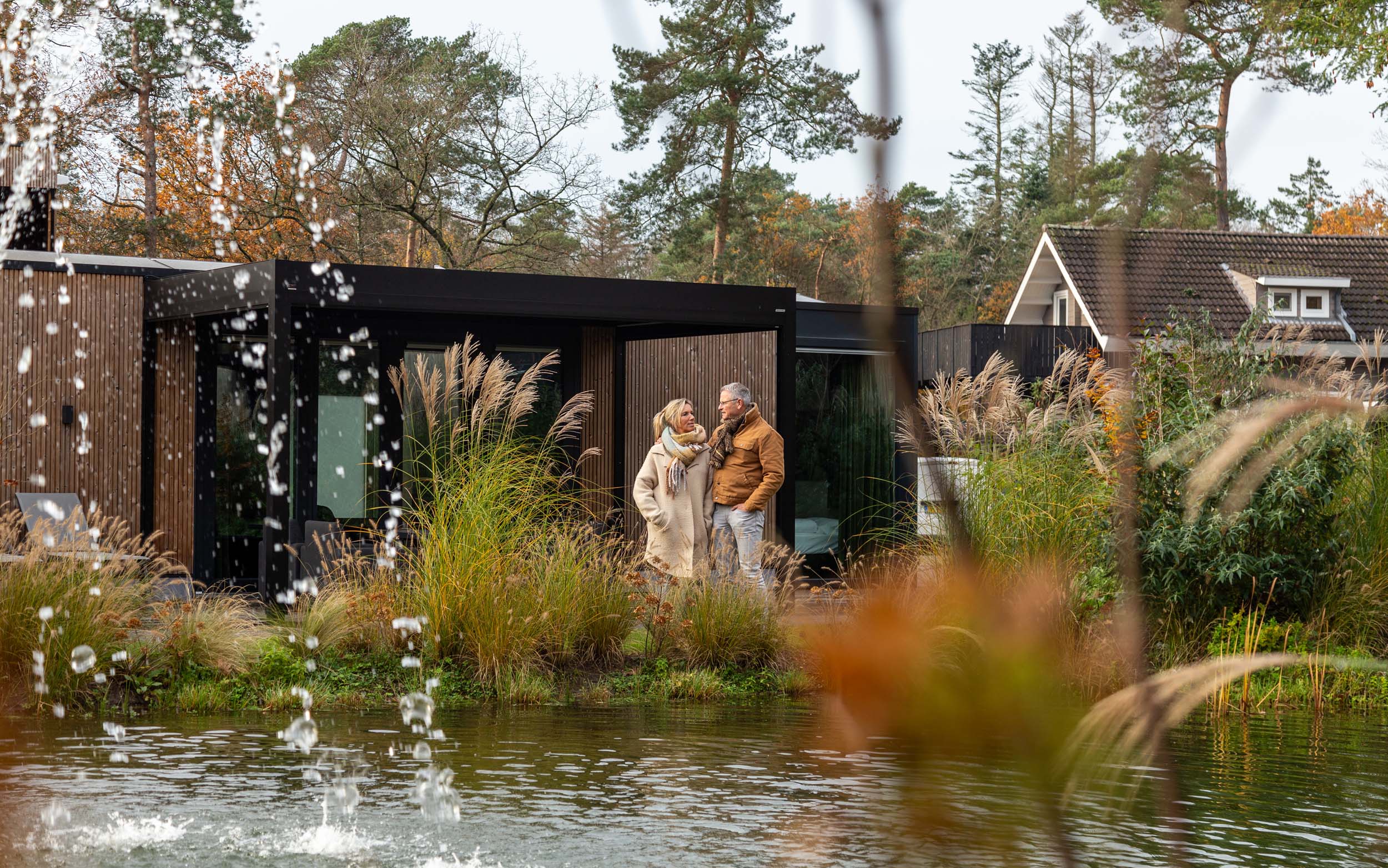 Een man en een vrouw staan voor een houten vakantiehuisje aan het water.