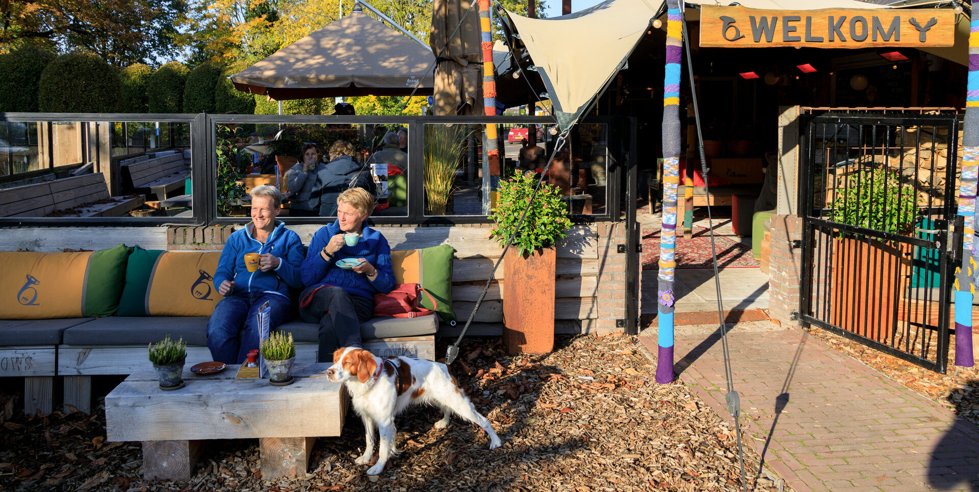 mensen die samen met hun hond buiten op het terras bij restaurant De Waldhoorn een drankje drinken