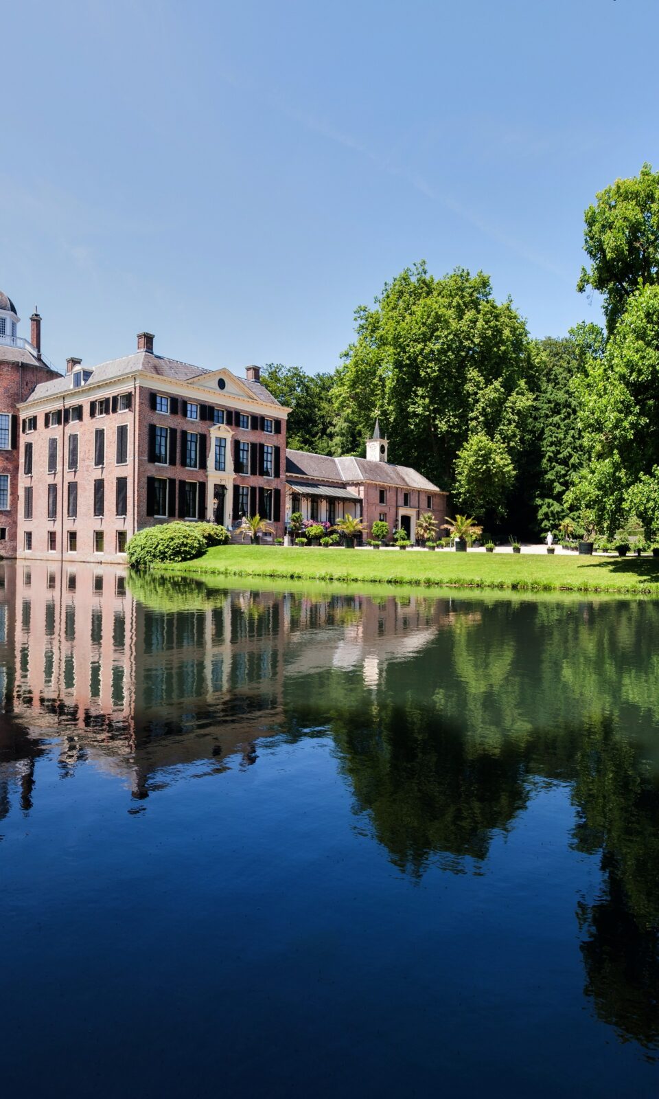 Kasteel Rosendael met een vijver ervoor, omringd door groen en een heldere lucht.