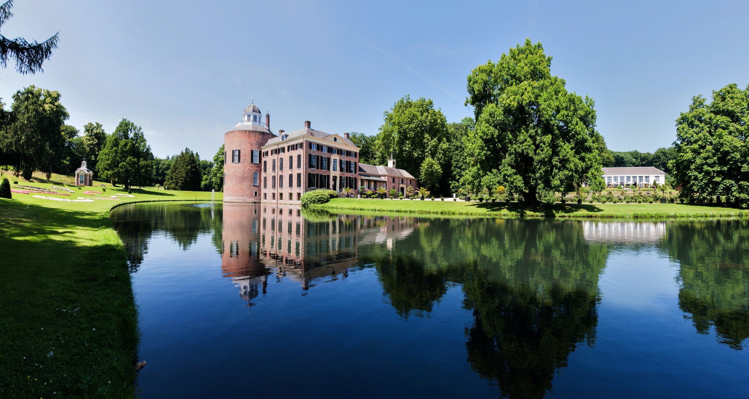 Kasteel Rosendael met een vijver ervoor, omringd door groen en een heldere lucht.