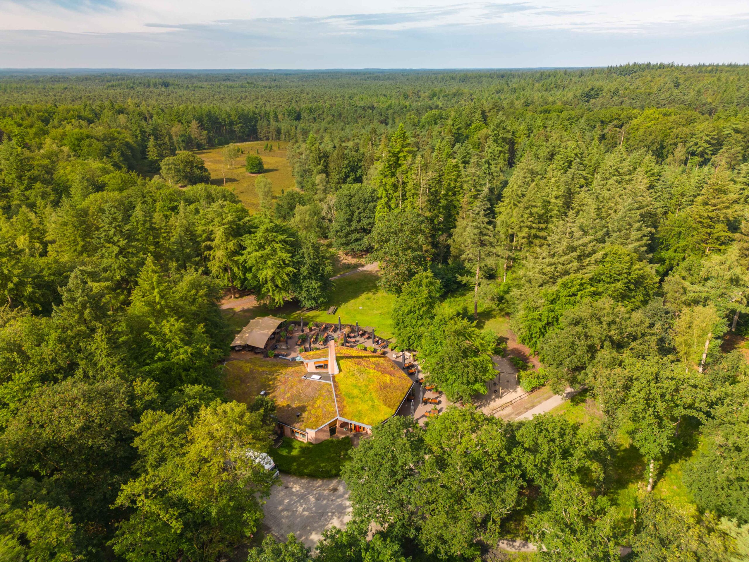 Dronefoto van een horecalocatie met terras dat middenin de groene bossen ligt