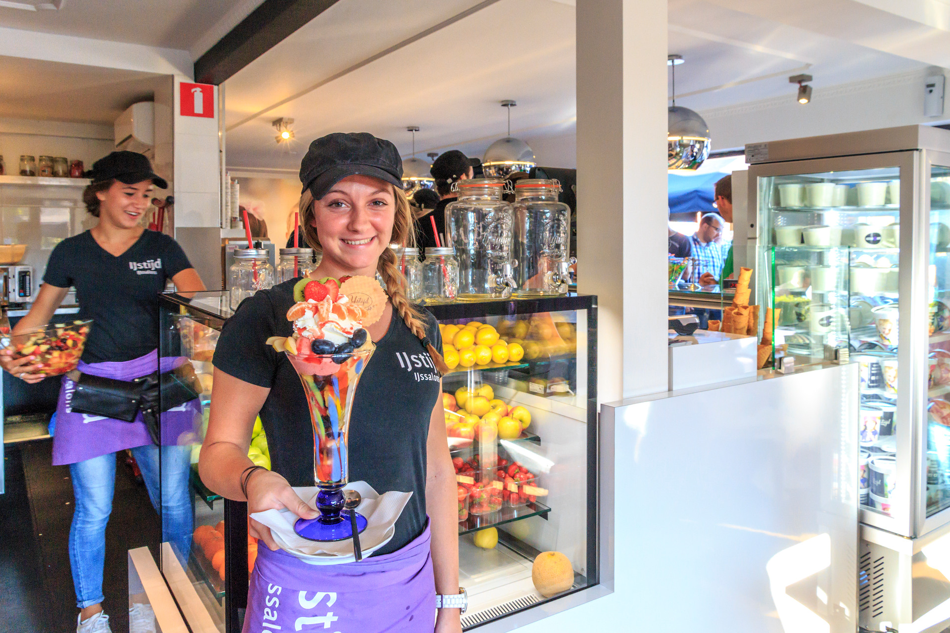 Vrouw met grote ijscoupe in haar handen die staat in een ijssalon