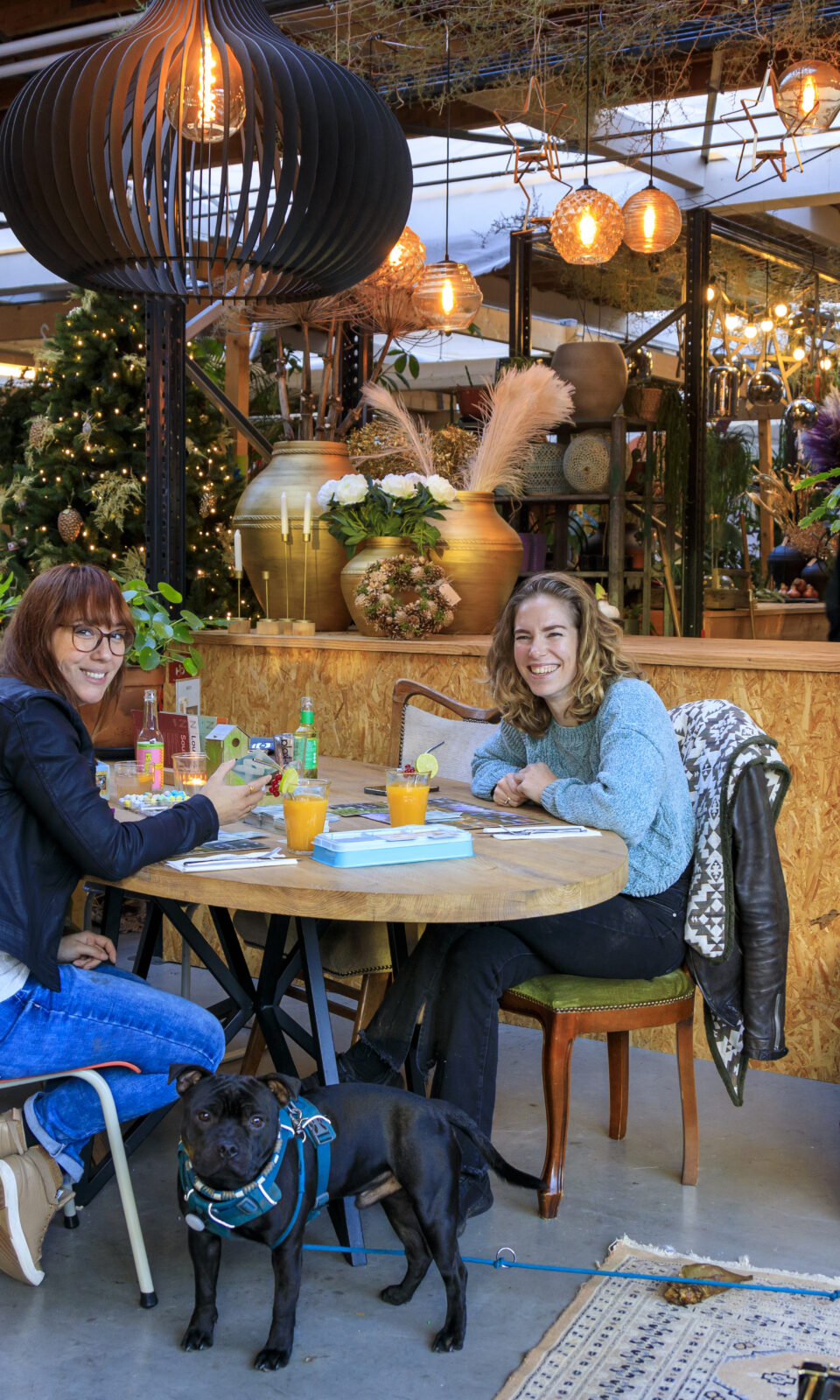 Twee vrouwen die aan een tafeltje zitten met een zwarte hond die voor de tafel staat